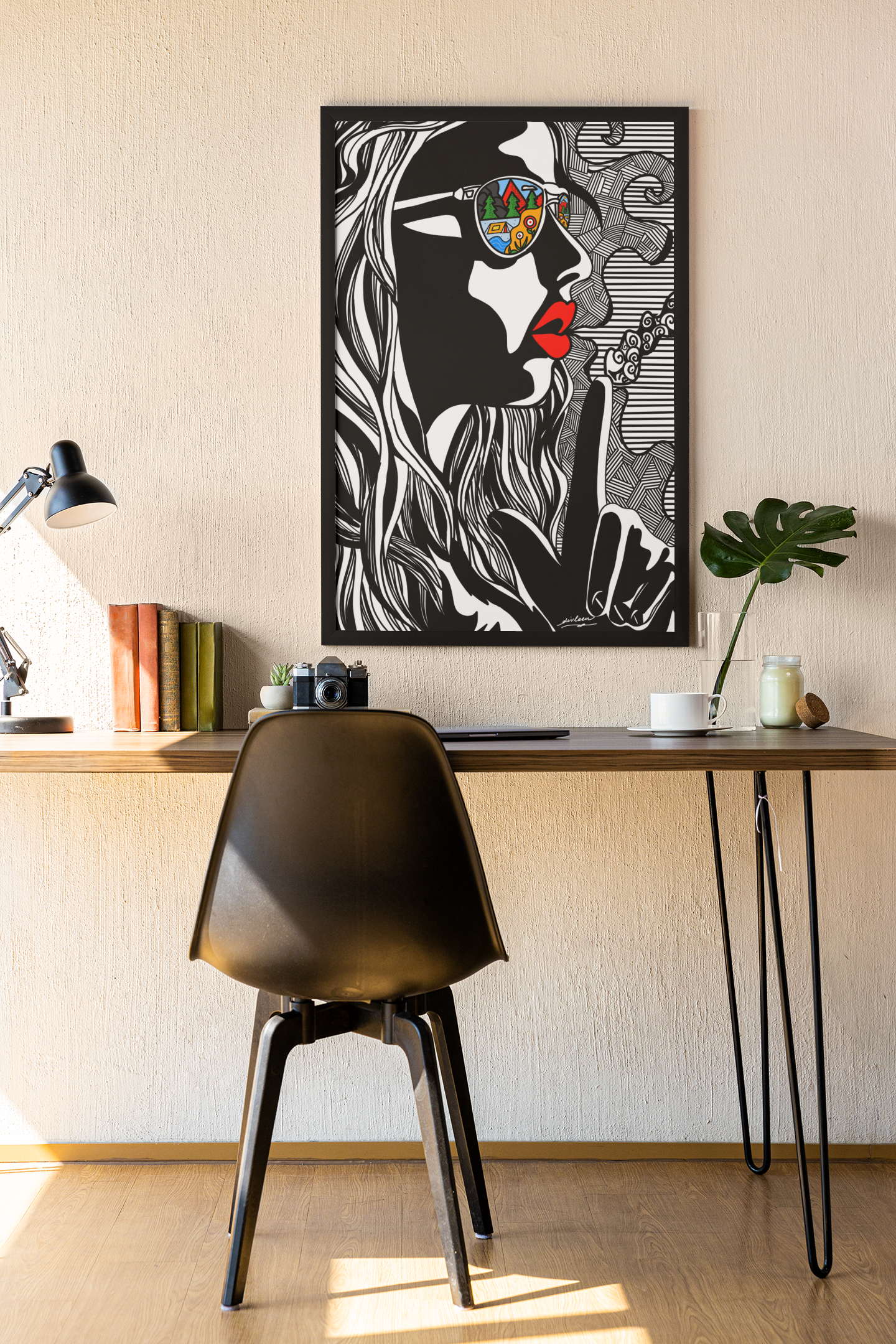 Modern workspace with black chair, wooden desk, lamp, books, camera, plant, and bold wall art of a woman in sunglasses
