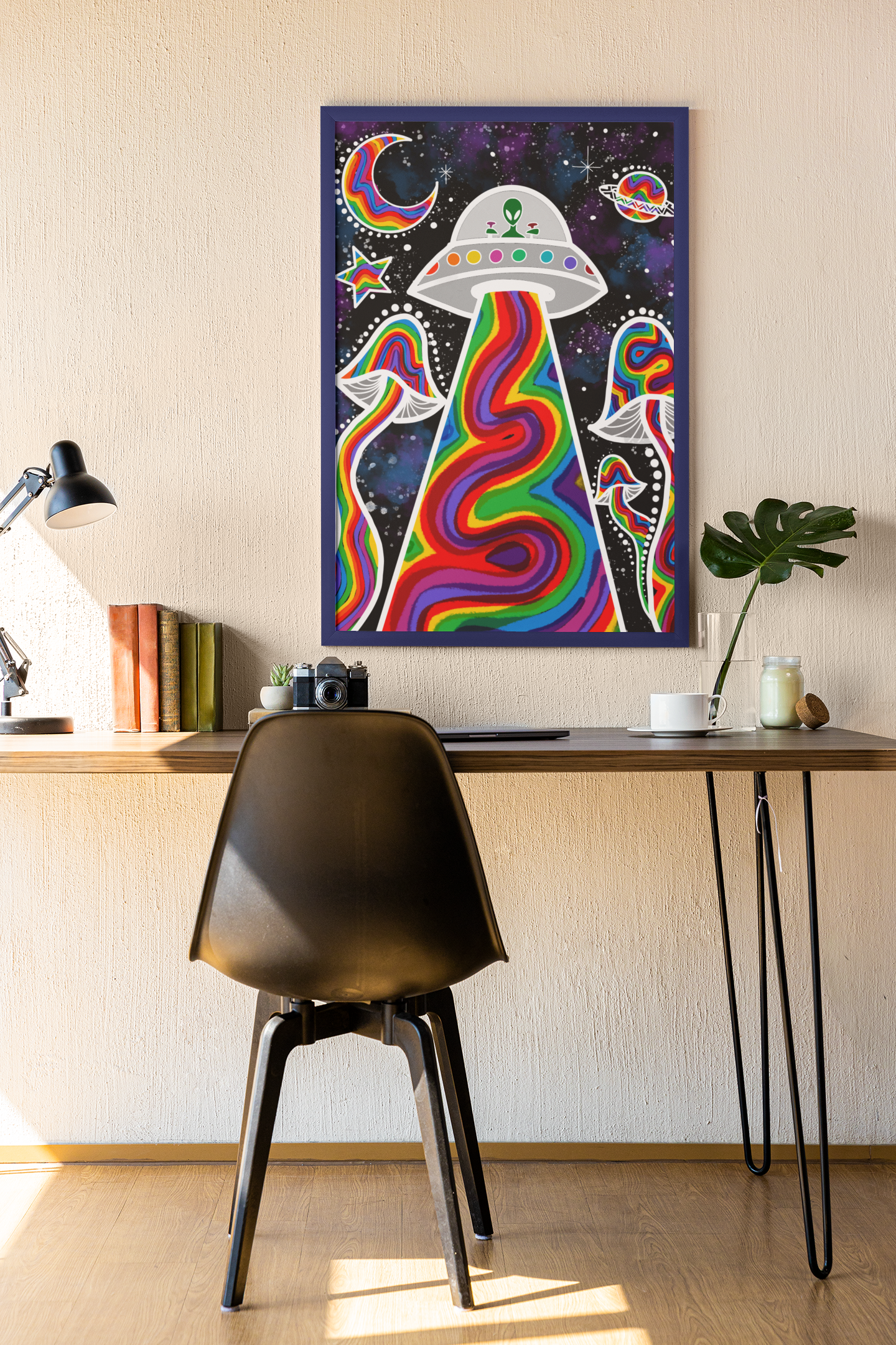 Framed psychedelic alien abduction art with rainbow beam, mushrooms, and space elements on wall above wooden desk