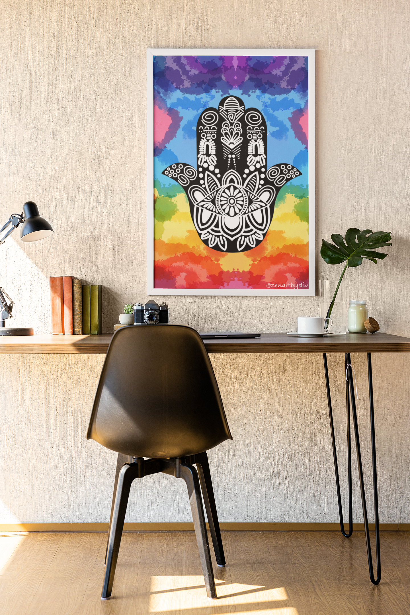 Black Hamsa hand with white intricate patterns on rainbow watercolor background framed on a beige wall above a wooden desk